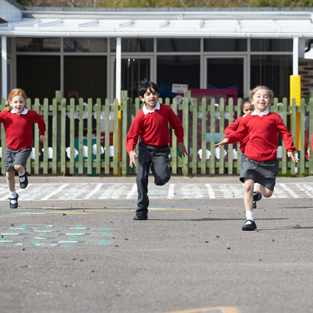 Primary school children in red uniforms running joyfully across a school playground
